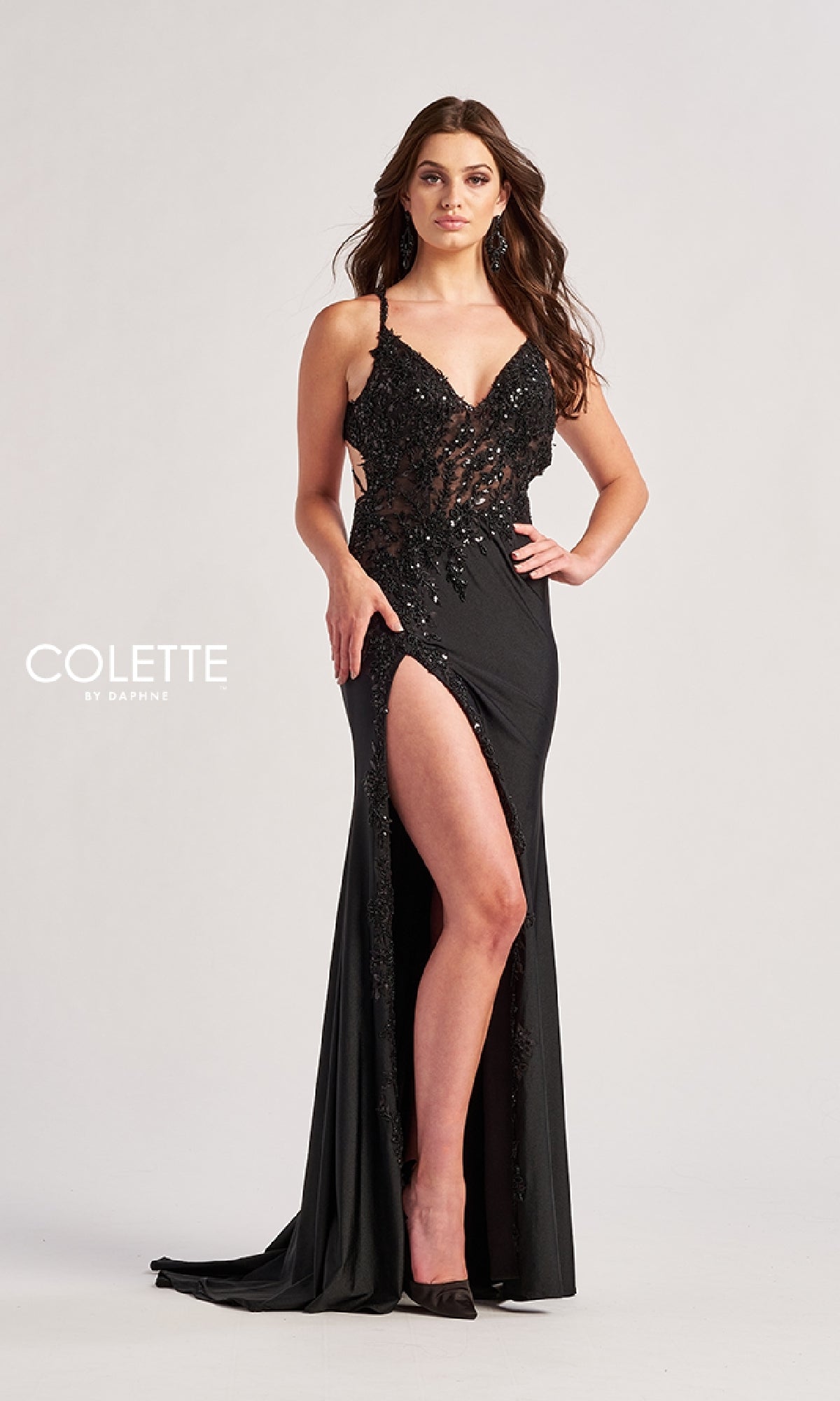 A woman stands against a plain light background wearing the Colette CL8535, a black long prom dress featuring a high slit, lace embroidery, spaghetti straps, an open back, and a floor-length silhouette.